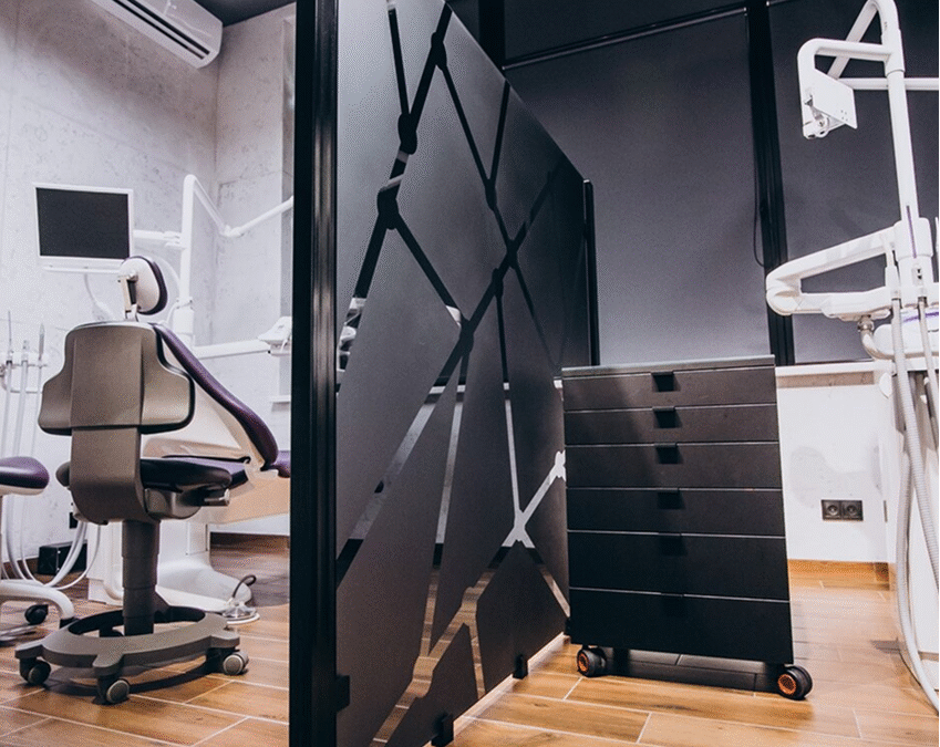 Modern dental clinic room with treatment chair, equipment, and privacy divider.